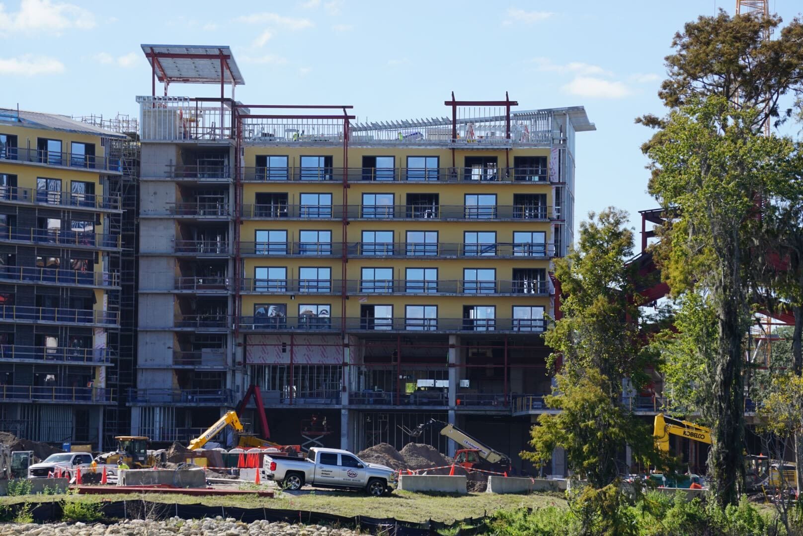 Lakeshore Update: A multi-story building under construction with cranes, trucks, workers, and trees—no Disney castle visible. Lakeshore Update: A multi-story building under construction with cranes, trucks, workers, and trees—no Disney castle visible.