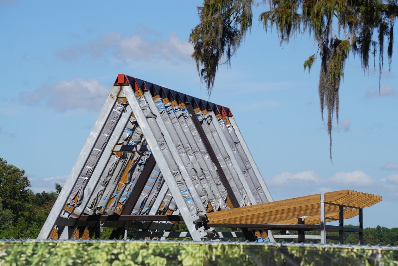 A-frame metal structure rising by a lakeshore, reminiscent of Disney's Polynesian Resort, framed by blue sky and draping moss. A-frame metal structure rising by a lakeshore, reminiscent of Disney's Polynesian Resort, framed by blue sky and draping moss.