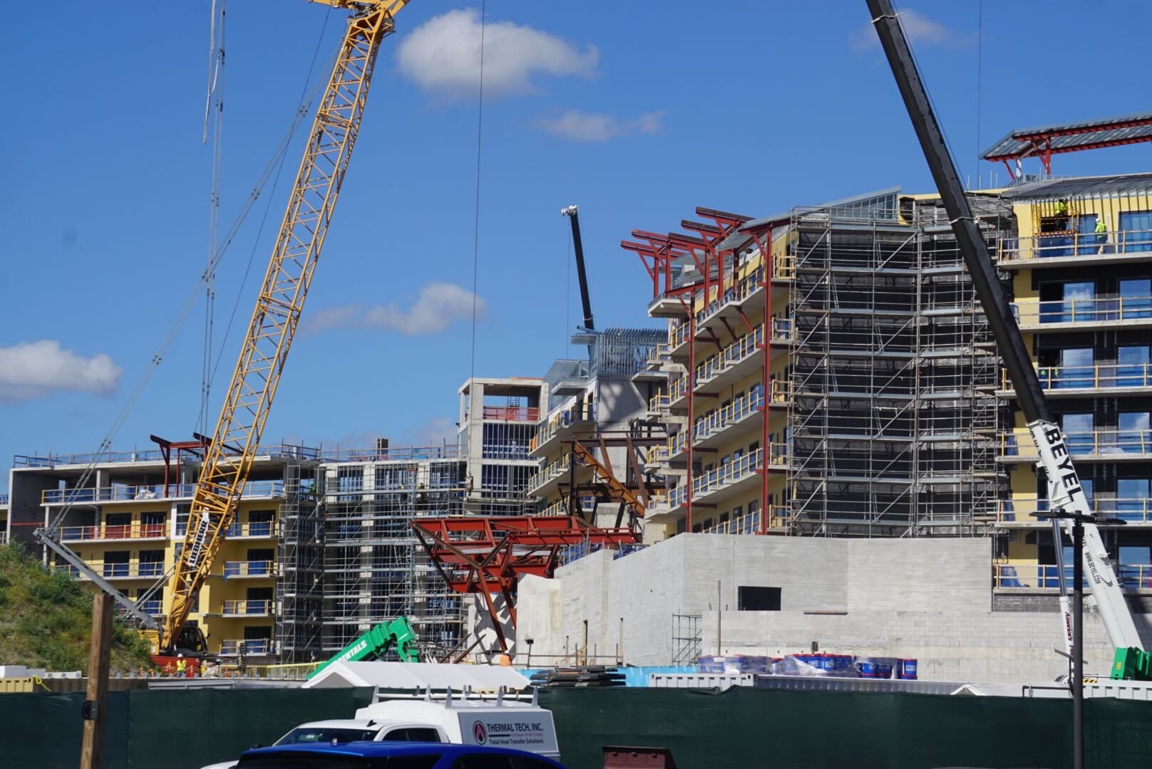 Construction site with cranes and scaffolding around multi-story buildings, reminiscent of Disney Parks expansions, under a blue sky. Construction site with cranes and scaffolding around multi-story buildings, reminiscent of Disney Parks expansions, under a blue sky.