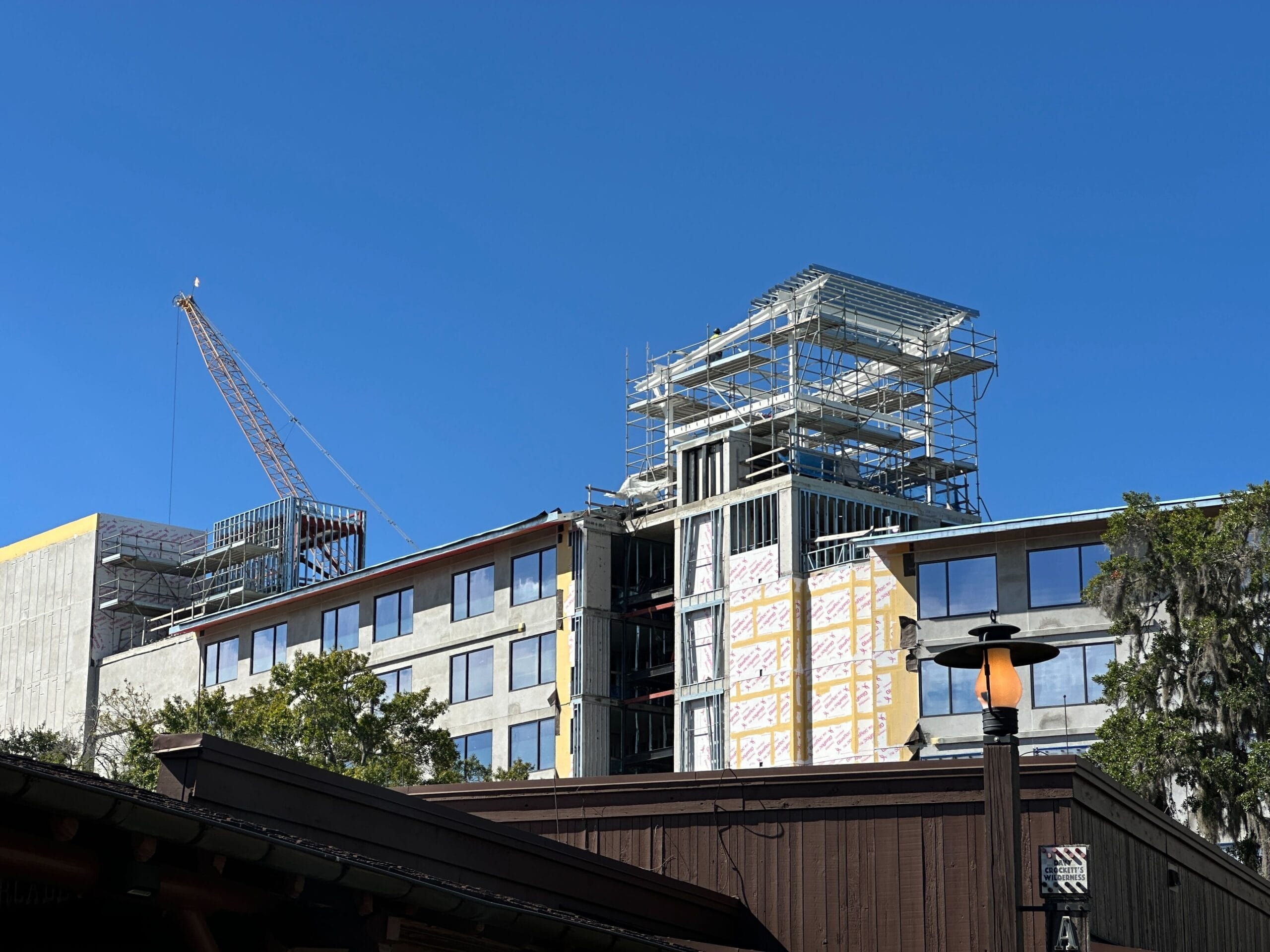 A building under construction with scaffolding and a crane, reminiscent of Disney parks' ongoing expansions, beneath a clear blue sky. A building under construction with scaffolding and a crane, reminiscent of Disney parks' ongoing expansions, beneath a clear blue sky.