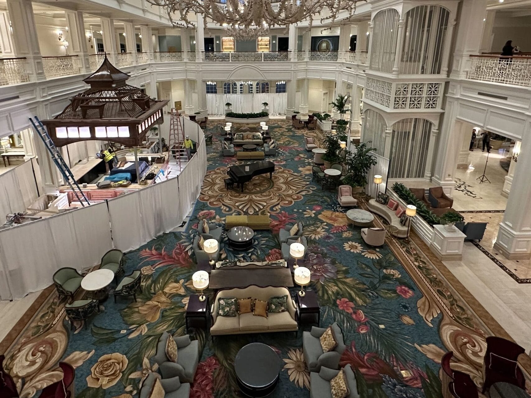 Grand hotel lobby reminiscent of Disney resort elegance, large chandelier, floral carpet, white railings, and plush seating areas. Grand hotel lobby reminiscent of Disney resort elegance, large chandelier, floral carpet, white railings, and plush seating areas.