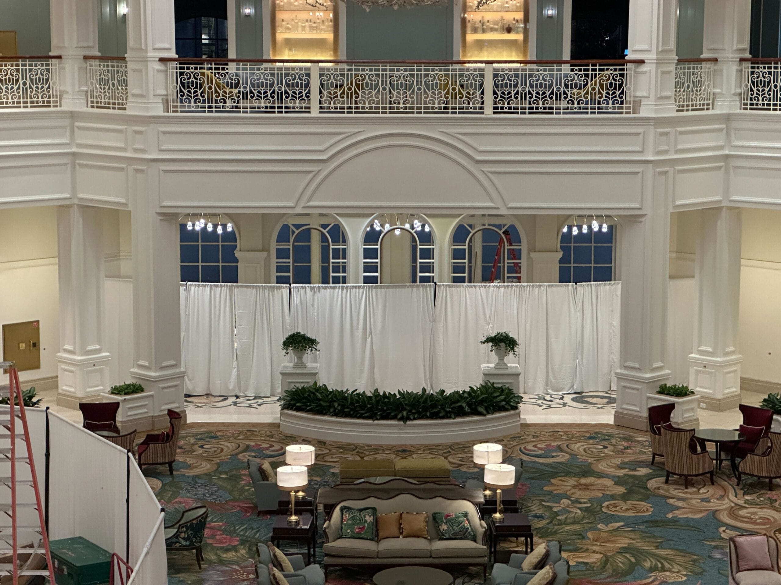 Elegant hotel lobby with white railings, chandeliers, floral carpet, and seating—reminiscent of Disney’s Grand Floridian Resort. Elegant hotel lobby with white railings, chandeliers, floral carpet, and seating—reminiscent of Disney’s Grand Floridian Resort.