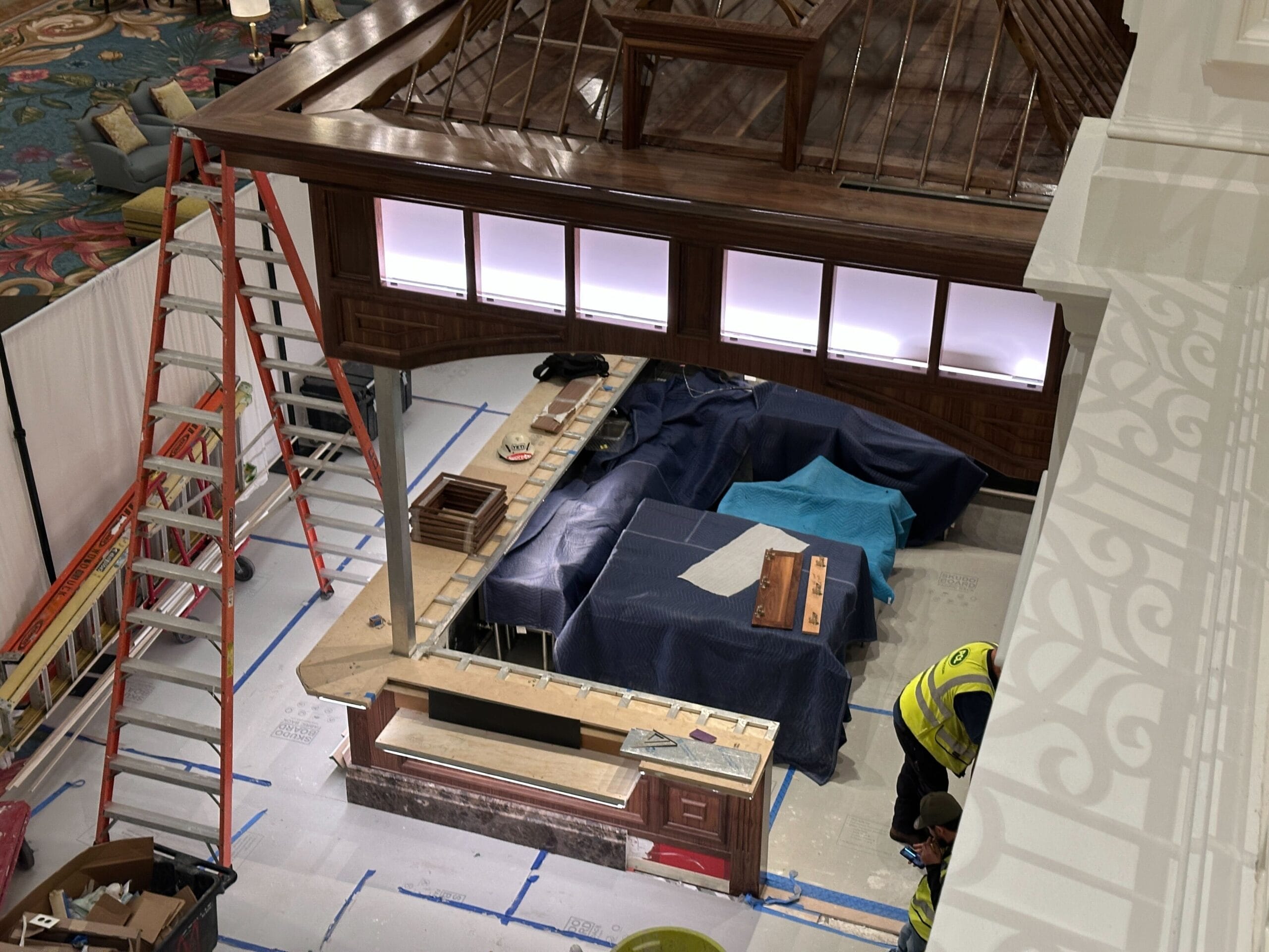 A construction zone in a Disney park with a wooden kiosk, tools, ladders, and workers in safety vests on a taped-off floor. A construction zone in a Disney park with a wooden kiosk, tools, ladders, and workers in safety vests on a taped-off floor.