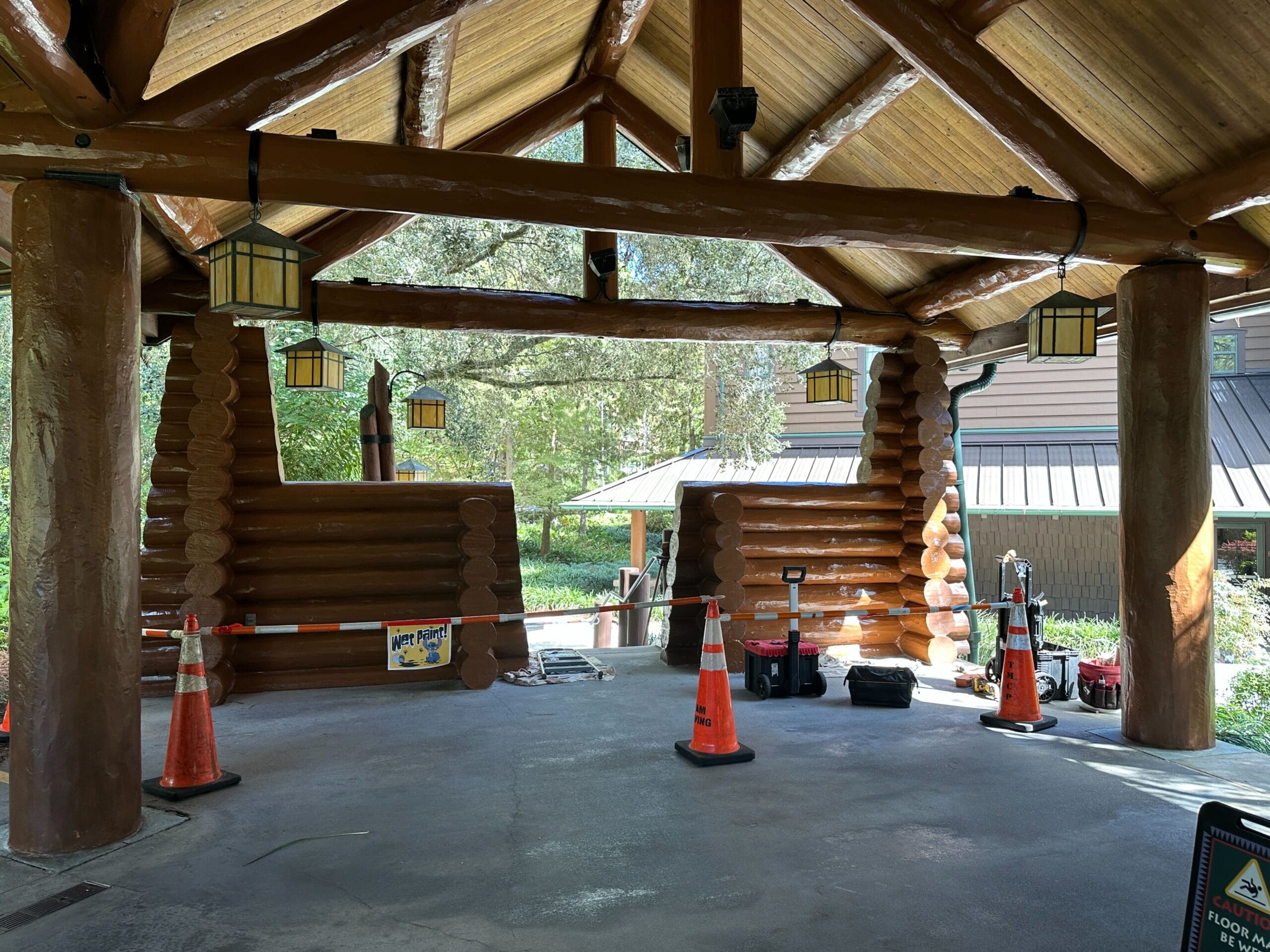 Rustic log cabin pavilion with orange cones, tools, and lanterns; lush greenery evokes Frontierland ambiance at Disney parks. Rustic log cabin pavilion with orange cones, tools, and lanterns; lush greenery evokes Frontierland ambiance at Disney parks.