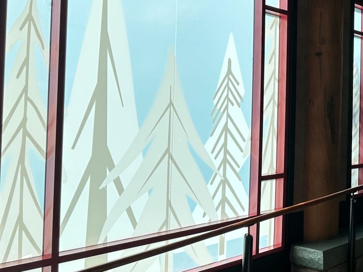 Guests stroll along a wooden hallway with frosted tree designs on the windows, sunlight streaming in like at Disney’s Wilderness Lodge. Guests stroll along a wooden hallway with frosted tree designs on the windows, sunlight streaming in like at Disney’s Wilderness Lodge.