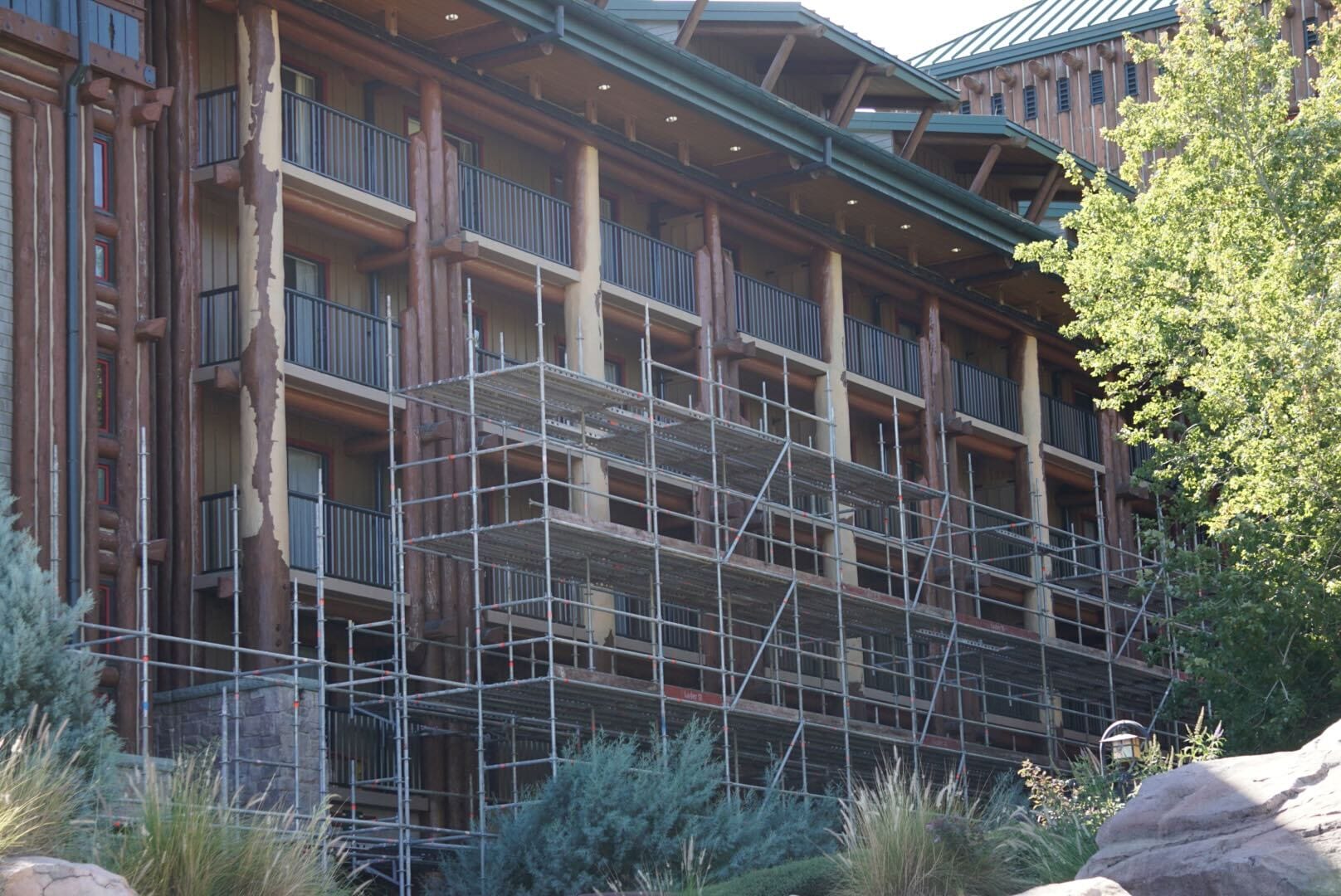 Scaffolding covers a multi-story lodge with balconies, surrounded by greenery, resembling Disney’s Wilderness Lodge at Walt Disney World. Scaffolding covers a multi-story lodge with balconies, surrounded by greenery, resembling Disney’s Wilderness Lodge at Walt Disney World.