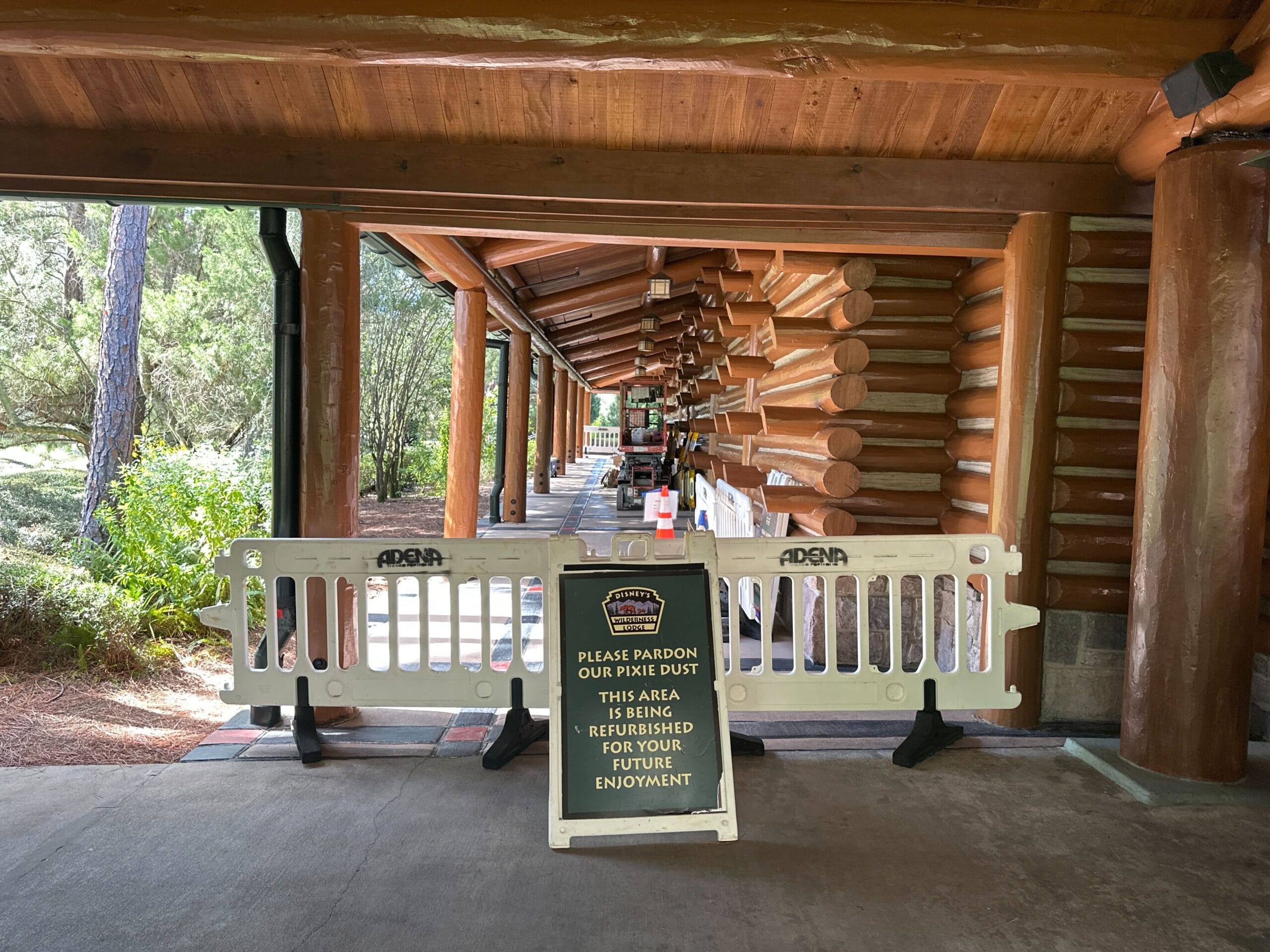 White construction barriers block a wooded walkway in a Disney park, with a sign about refurbishment for future guest enjoyment. White construction barriers block a wooded walkway in a Disney park, with a sign about refurbishment for future guest enjoyment.