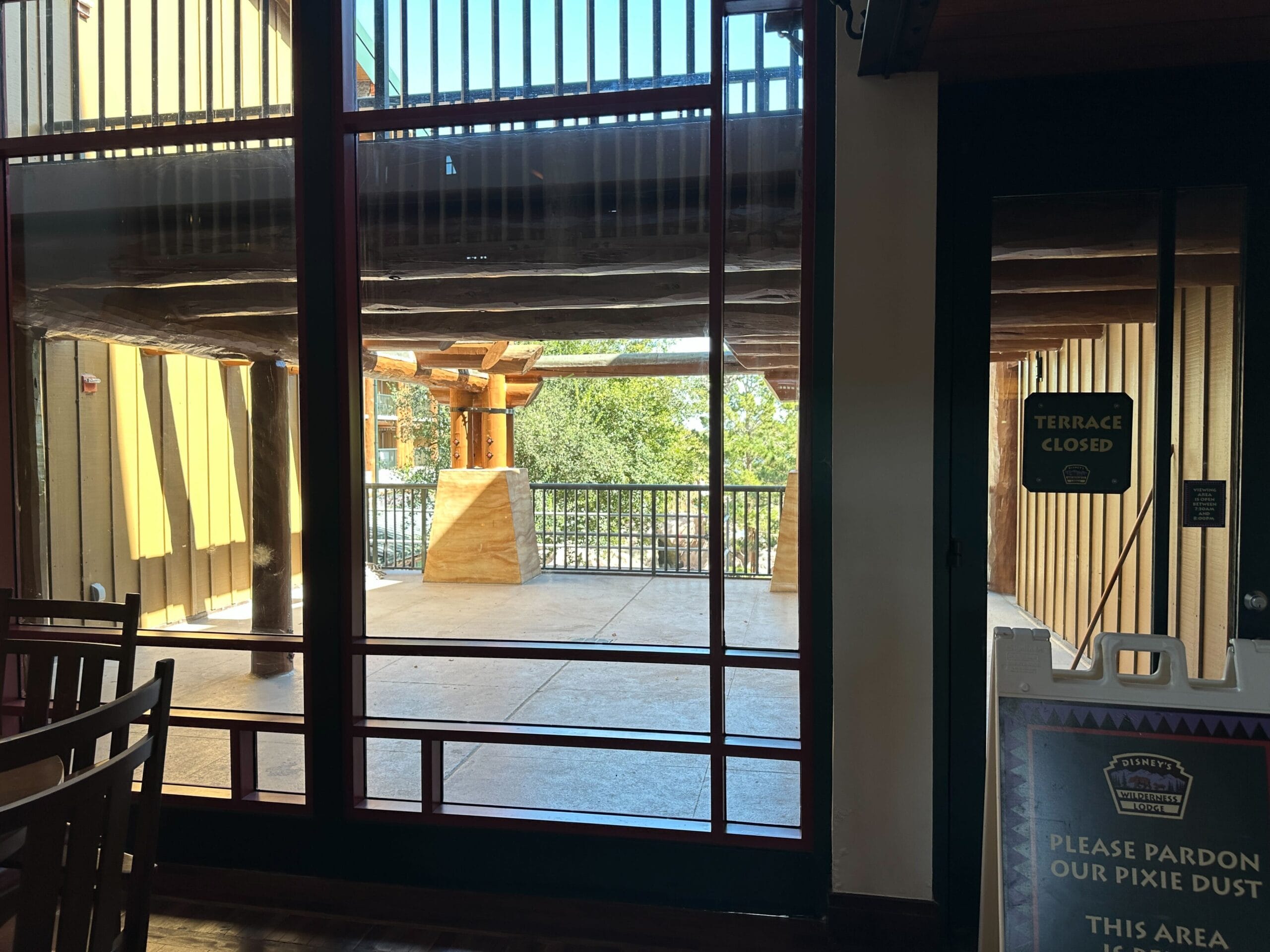 A sunlit terrace at a Disney park is closed off behind glass doors, with a Terrace Closed sign and construction notice visible. A sunlit terrace at a Disney park is closed off behind glass doors, with a Terrace Closed sign and construction notice visible.