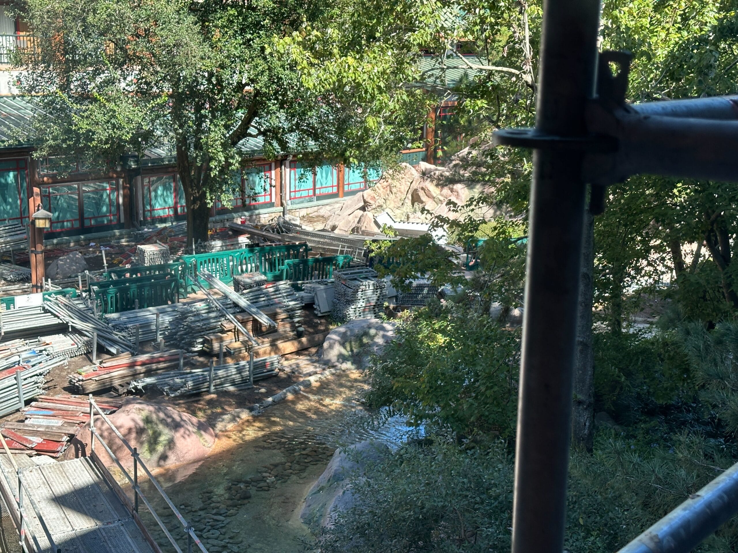 Construction site with stacked metal pipes and green fencing near trees and a building, resembling Epcot construction areas in Disney Parks. Construction site with stacked metal pipes and green fencing near trees and a building, resembling Epcot construction areas in Disney Parks.