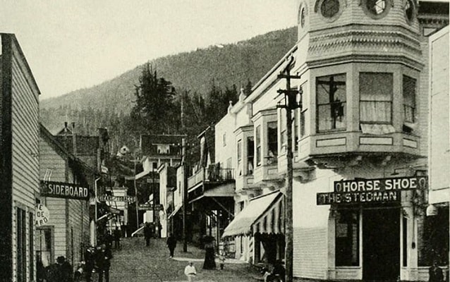 Black and white photo of a street lined with shops with mountains in background. Black and white photo of a street lined with shops with mountains in background.