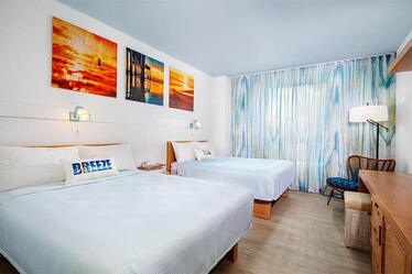 Side view of standard room at Endless Summer Resort - Dockside Inn and Suites with two queen beds, a desk and pictures of sunlit waters.